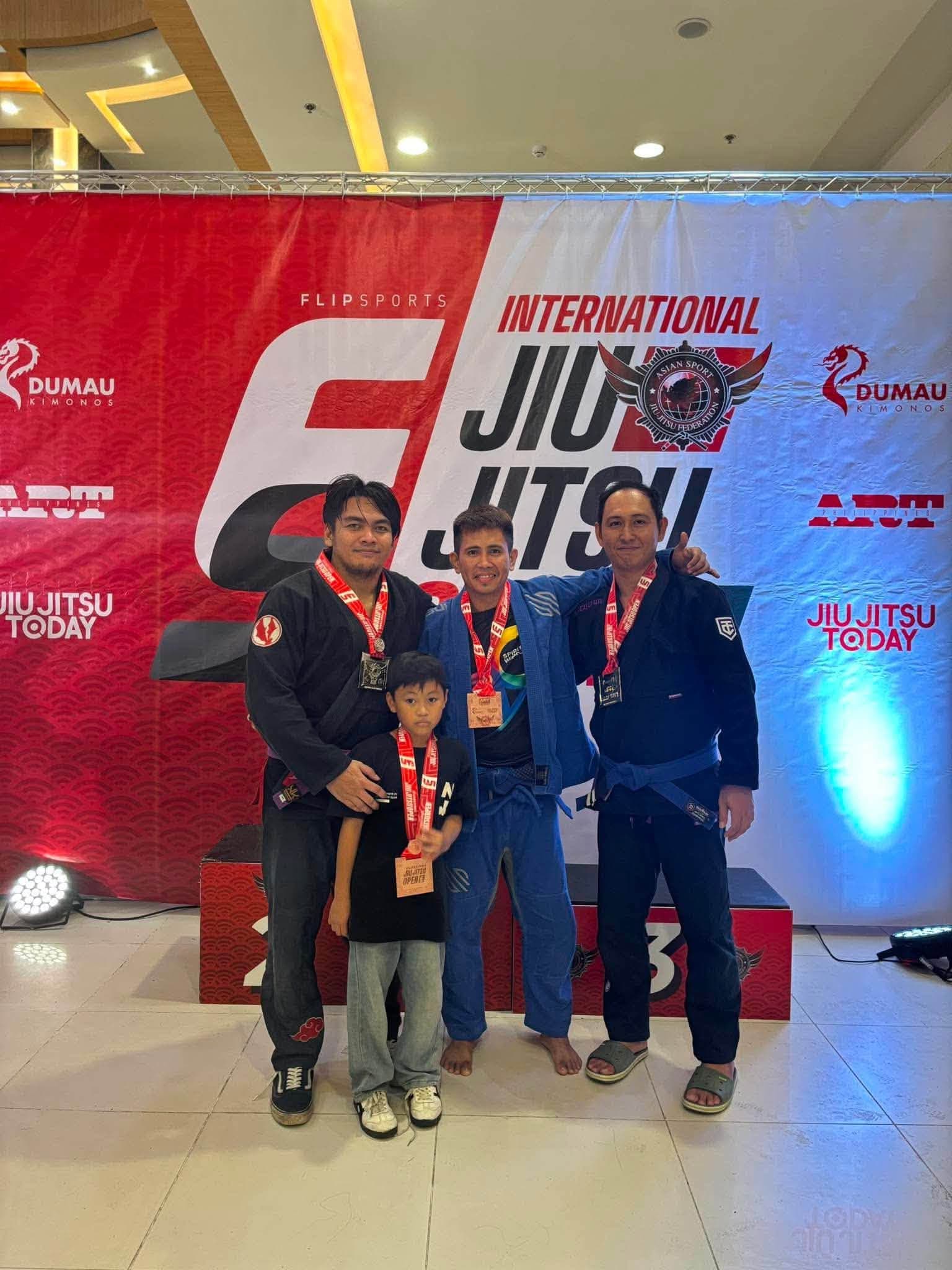 Kabkad athletes wearing their medals in front of the Flipsports International Jiu Jitsu Open banner